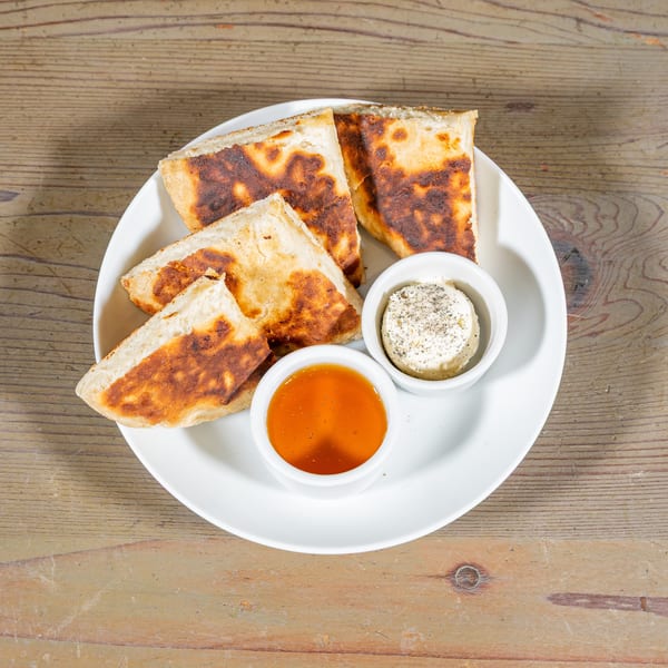 Golden brown flatbread pieces on a white plate with small bowls of honey and cream cheese.