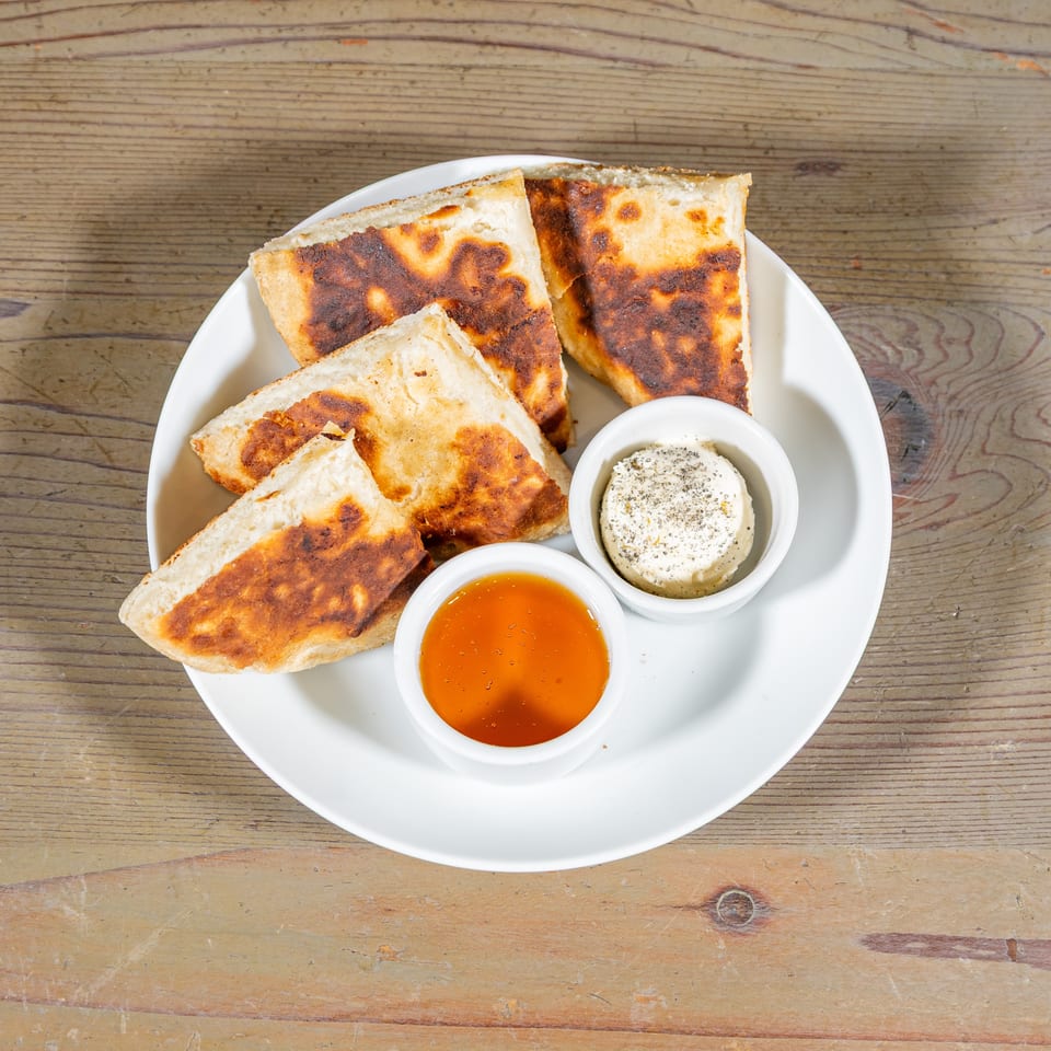Golden brown flatbread pieces on a white plate with small bowls of honey and cream cheese.