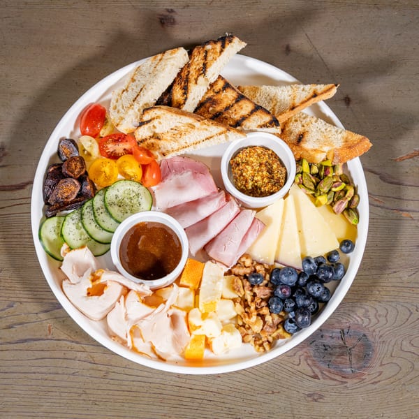 A charcuterie board with grilled bread, meats, cheeses, fruits, vegetables, and dipping sauces.