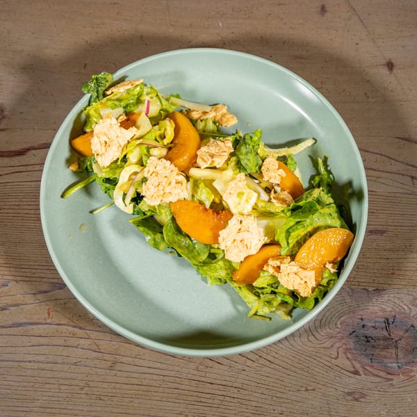 A vibrant green salad with orange peach slices and crispy croutons on a light blue plate.