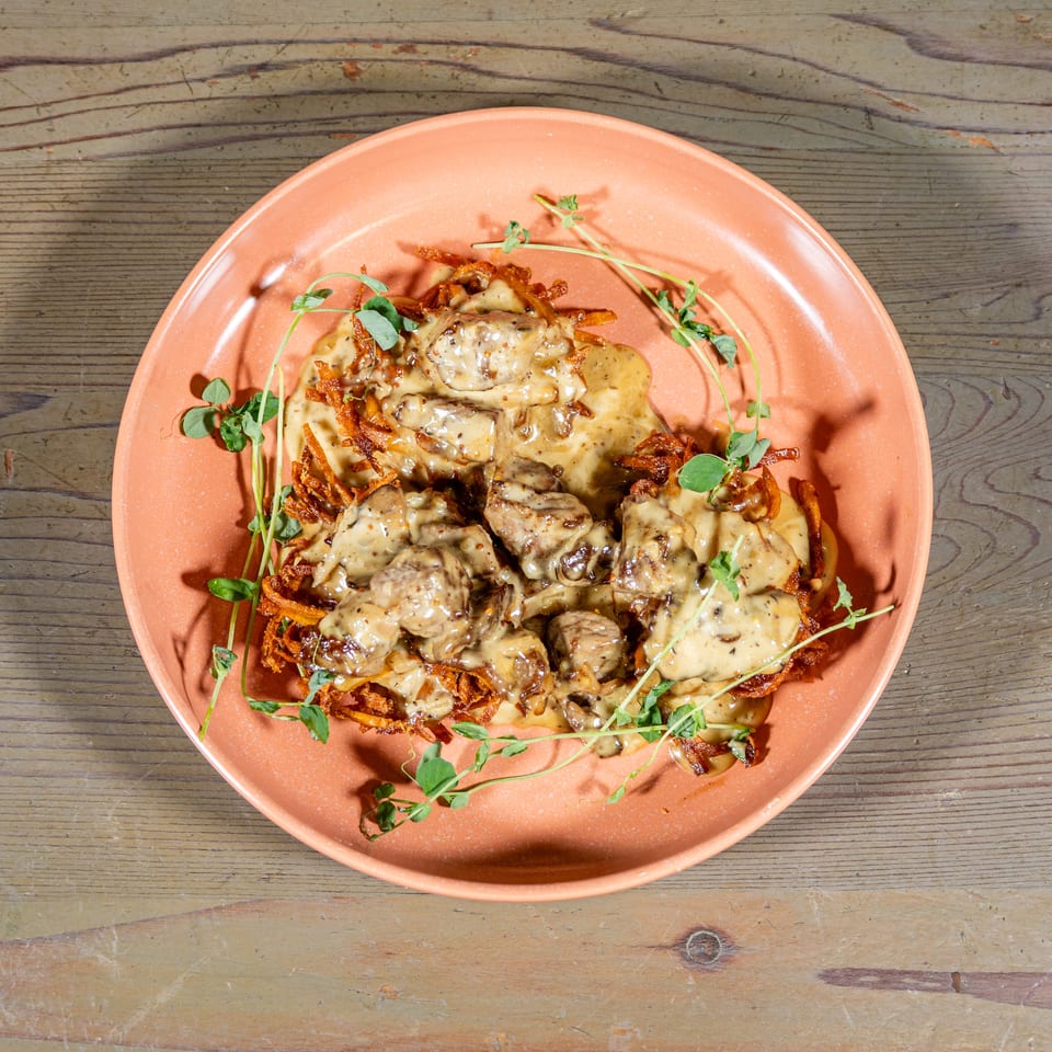 Savory dish with meat and creamy sauce on crispy potato pancakes, garnished with fresh herbs.