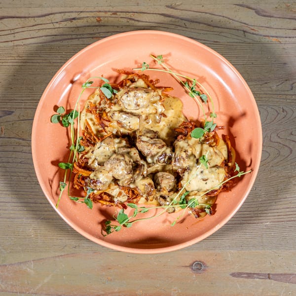 Savory dish with meat and creamy sauce on crispy potato pancakes, garnished with fresh herbs.