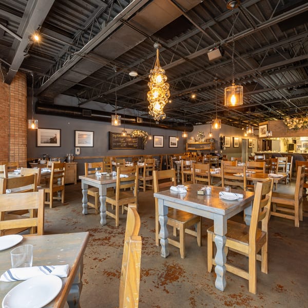 Spacious restaurant dining room with wooden tables and chairs, exposed brick, and industrial-chic lighting.