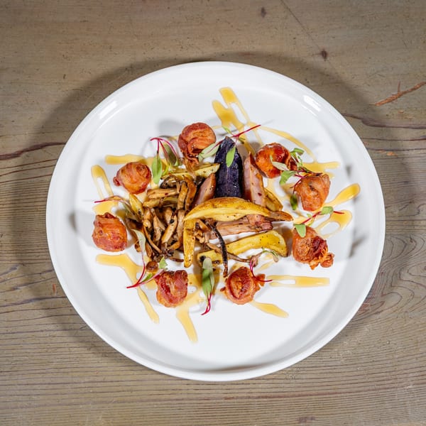 Gourmet dish with bacon-wrapped scallops, roasted vegetables, and mushrooms on a white plate.
