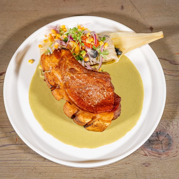 Crispy pork belly in green sauce with a tamale and corn salsa on a white plate.