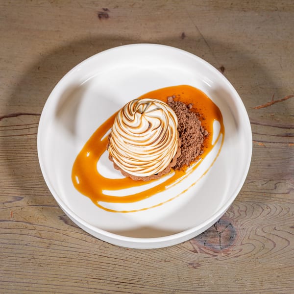 Chocolate tart with toasted meringue, caramel drizzle, and chocolate crumble on a white plate.