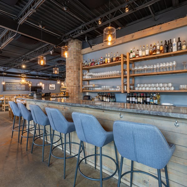 Inviting restaurant bar with blue stools, a wooden counter, and shelves stocked with bottles and glasses.