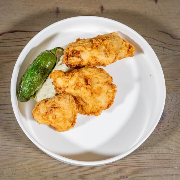 Three pieces of crispy fried chicken, mashed potatoes, and a roasted green pepper on a white plate.