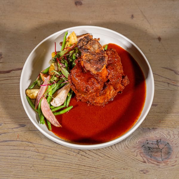 Rich braised meat in red sauce, served with green beans and roasted potatoes on a wooden table.