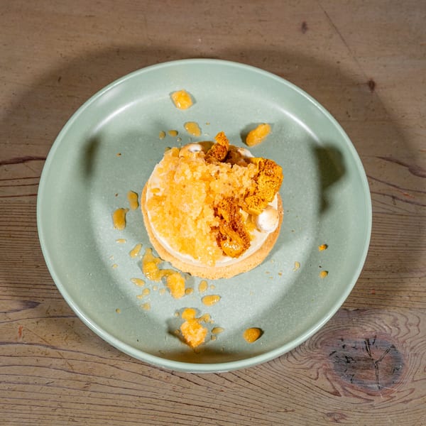 A dessert with white cream, orange crumble, and honeycomb on a light green plate.