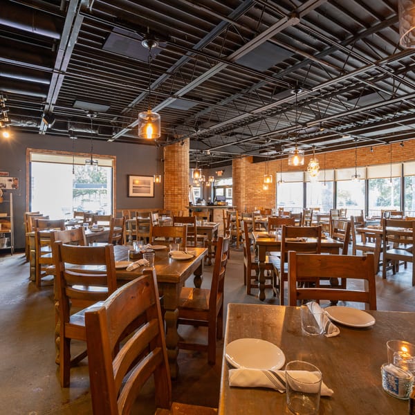 Spacious restaurant dining room with wooden tables and chairs, exposed brick, and industrial lighting.