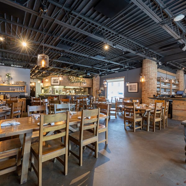 Inviting restaurant dining room with wooden tables, chairs, an open kitchen, and a bar under industrial lighting.