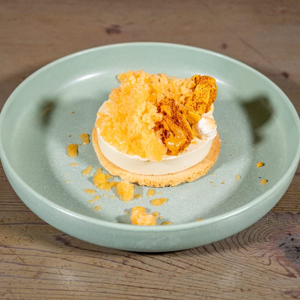A dessert with a white base, topped with orange crumble, honeycomb, and meringue on a green plate.