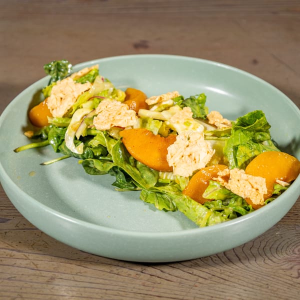 A vibrant green salad with orange fruit slices and crispy toppings in a light blue bowl.