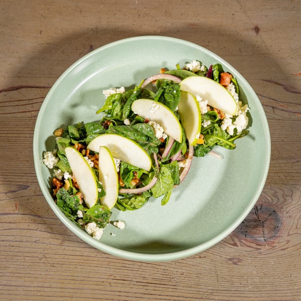 Spinach salad with apple slices, red onion, walnuts, and feta cheese on a light green plate.