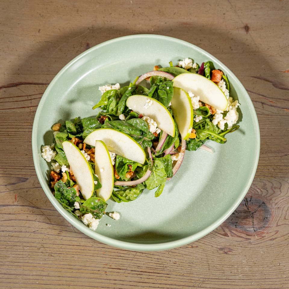 Spinach salad with apple slices, red onion, walnuts, and feta cheese on a light green plate.
